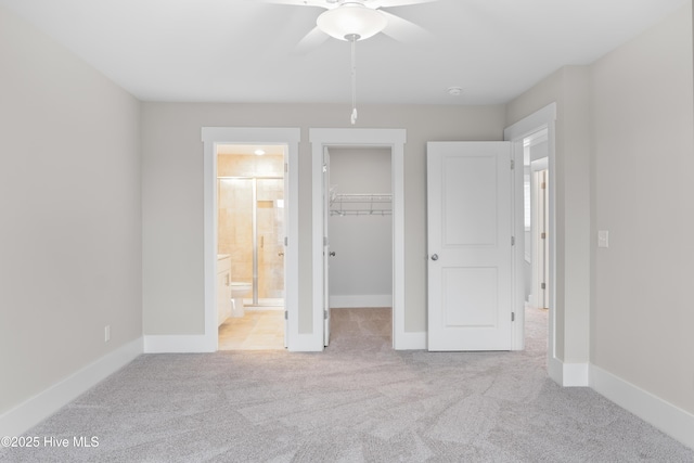 unfurnished bedroom featuring ensuite bath, light colored carpet, ceiling fan, a spacious closet, and a closet