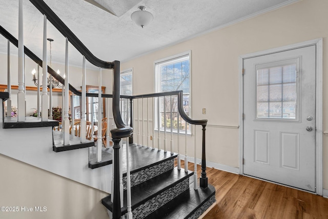 foyer with hardwood / wood-style flooring, ornamental molding, an inviting chandelier, and a textured ceiling