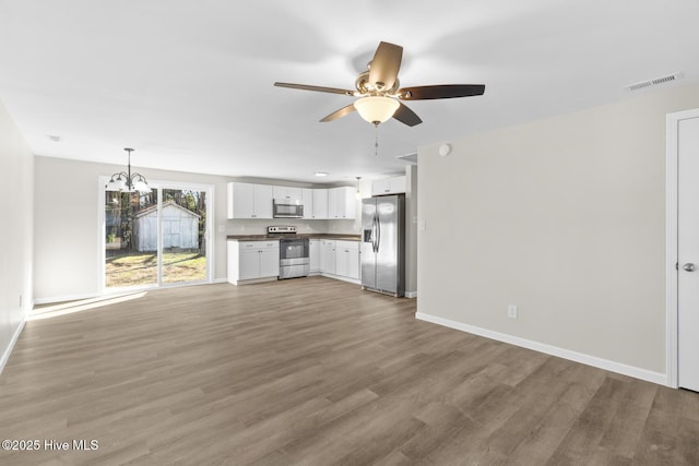 unfurnished living room featuring hardwood / wood-style floors and ceiling fan with notable chandelier