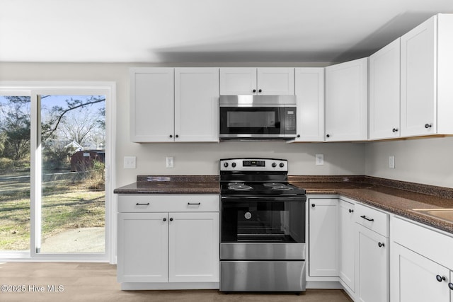 kitchen featuring light wood-type flooring, stainless steel appliances, white cabinetry, and dark stone countertops