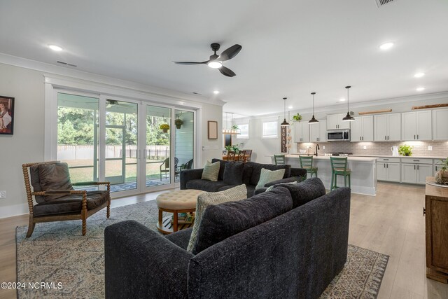 living room with ceiling fan, crown molding, and light hardwood / wood-style flooring