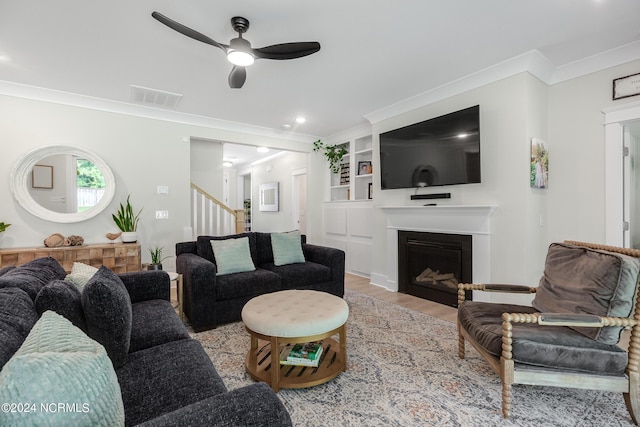 living room with built in shelves, ceiling fan, light wood-type flooring, and crown molding