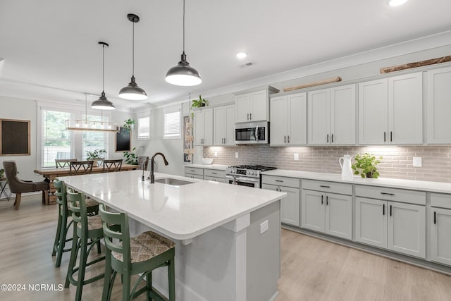 kitchen featuring hanging light fixtures, sink, an island with sink, appliances with stainless steel finishes, and a kitchen bar