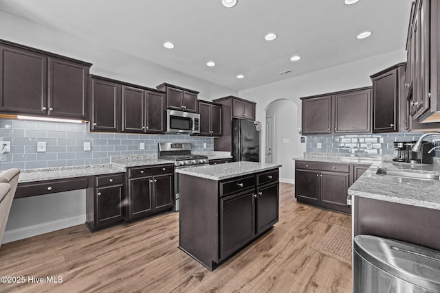 kitchen featuring appliances with stainless steel finishes, light wood-type flooring, light stone counters, sink, and a kitchen island