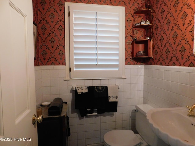 bathroom with toilet, sink, and tile walls