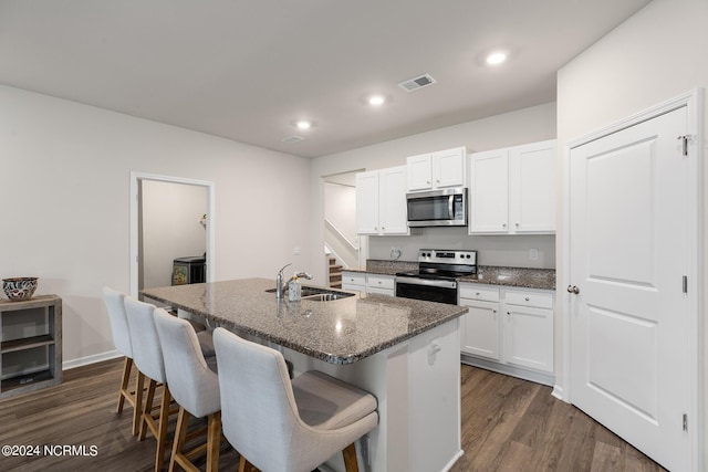 kitchen with white cabinets, sink, dark stone countertops, an island with sink, and appliances with stainless steel finishes