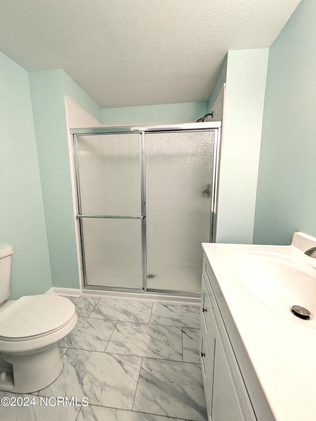 bathroom featuring vanity, a textured ceiling, toilet, and a shower with door