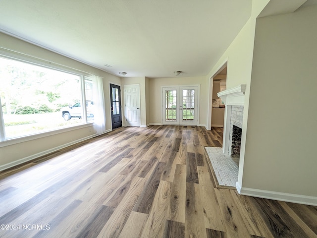 unfurnished living room with wood-type flooring, a brick fireplace, and french doors