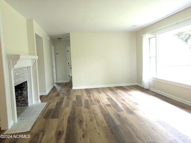 unfurnished living room with a wealth of natural light, dark hardwood / wood-style floors, and a brick fireplace