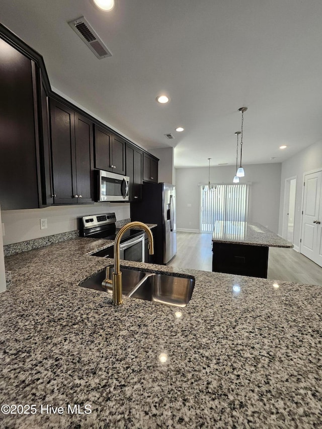 kitchen with a center island, stone counters, hanging light fixtures, sink, and appliances with stainless steel finishes