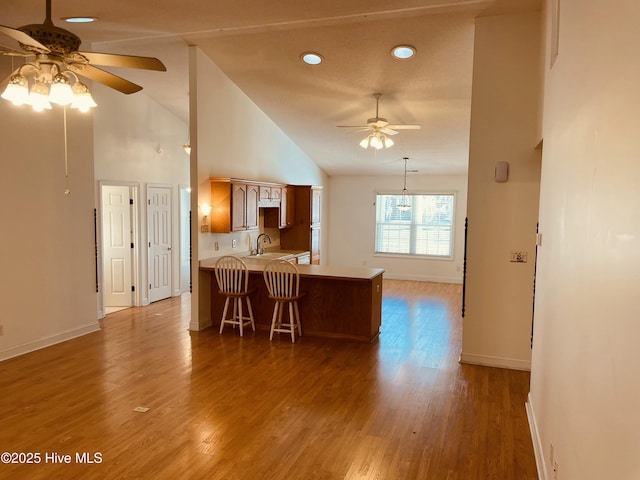 kitchen featuring kitchen peninsula, high vaulted ceiling, ceiling fan, and hardwood / wood-style flooring