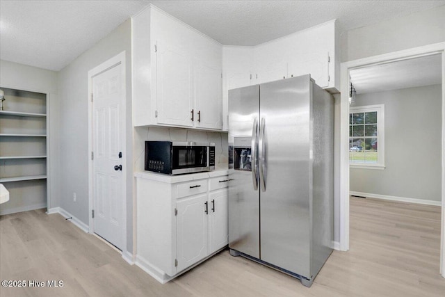 kitchen with a textured ceiling, light hardwood / wood-style flooring, white cabinets, and appliances with stainless steel finishes