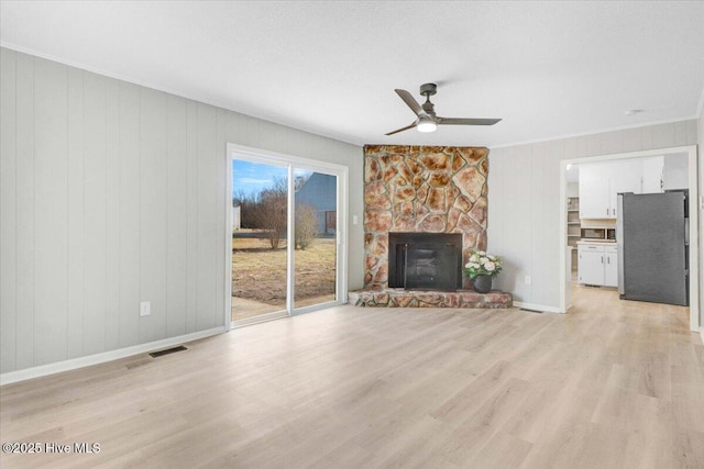 unfurnished living room with ceiling fan, ornamental molding, a fireplace, and light wood-type flooring