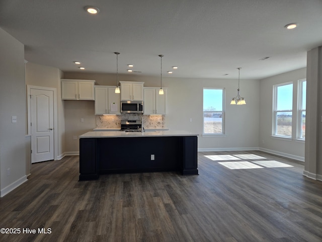 kitchen featuring backsplash, decorative light fixtures, stainless steel appliances, white cabinets, and a kitchen island with sink