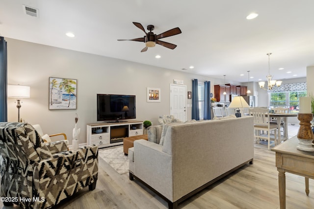 living room featuring ceiling fan with notable chandelier and light hardwood / wood-style flooring