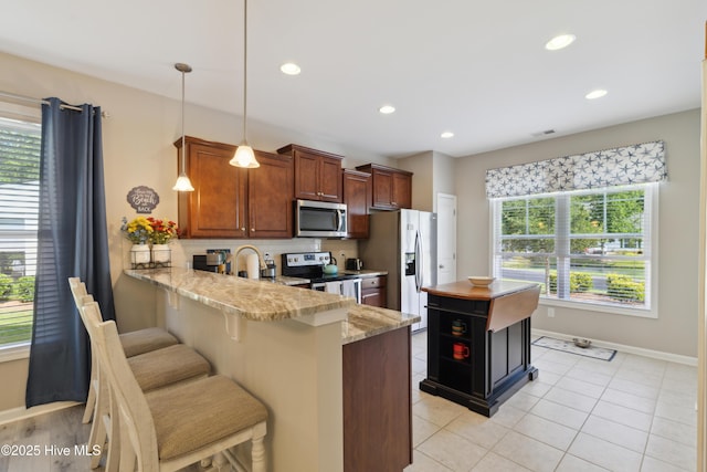 kitchen with pendant lighting, a breakfast bar, kitchen peninsula, plenty of natural light, and stainless steel appliances