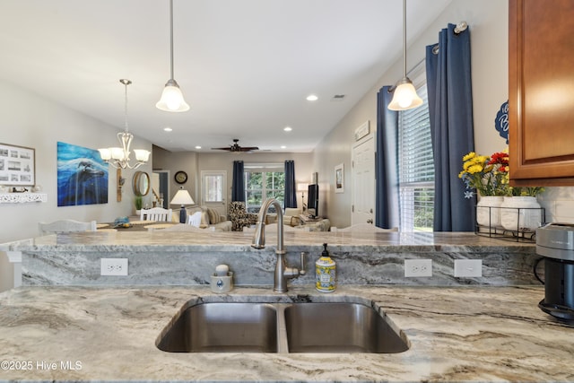 kitchen featuring decorative light fixtures, sink, light stone countertops, and ceiling fan with notable chandelier