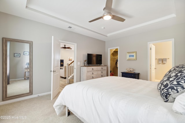 carpeted bedroom with ensuite bathroom, a walk in closet, a raised ceiling, and ceiling fan