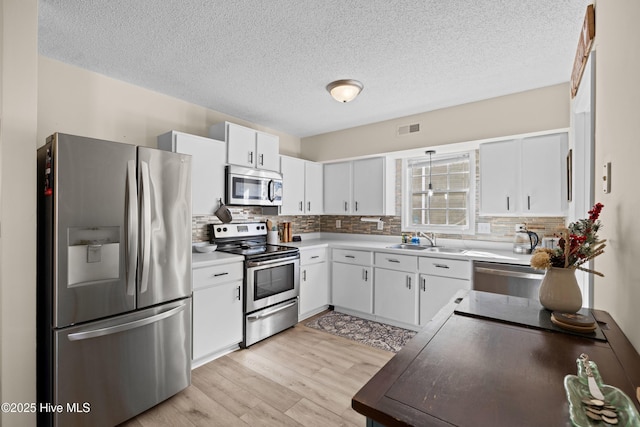 kitchen with white cabinets, sink, stainless steel appliances, and light hardwood / wood-style flooring