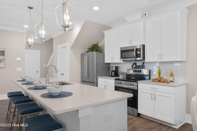 kitchen featuring hanging light fixtures, stainless steel appliances, white cabinets, and a kitchen island with sink