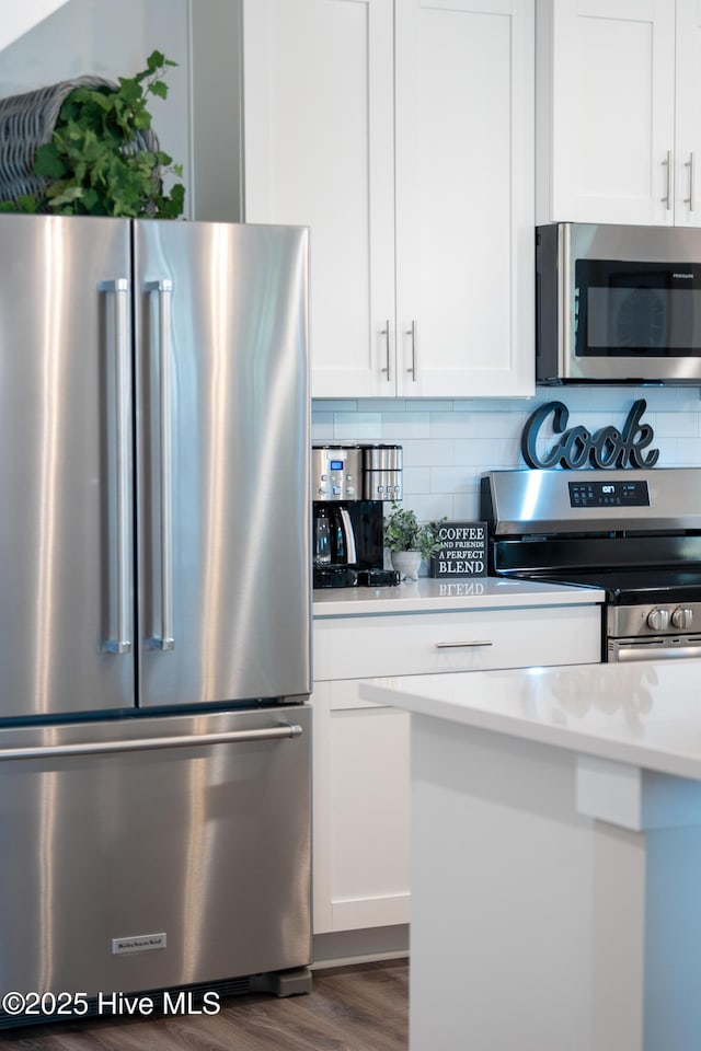 kitchen with appliances with stainless steel finishes, backsplash, white cabinetry, and dark wood-type flooring