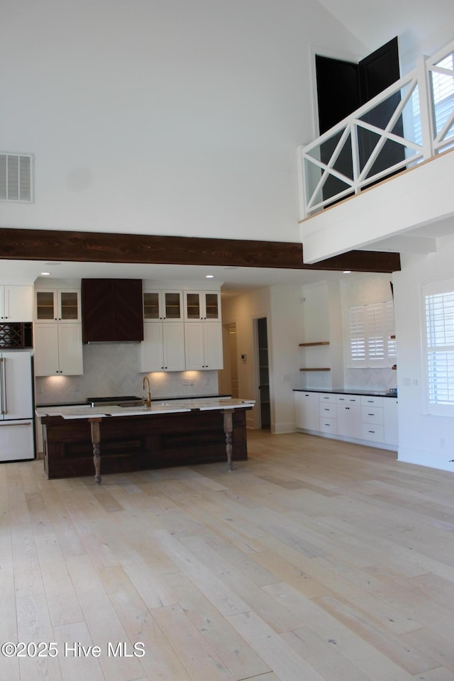 kitchen featuring white cabinetry, backsplash, fridge, a high ceiling, and light wood-type flooring