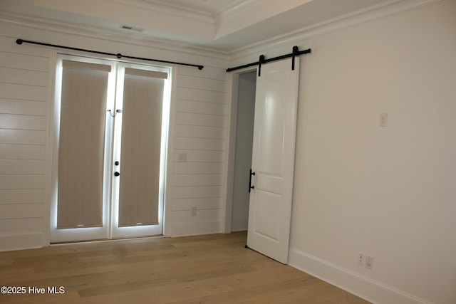 unfurnished bedroom featuring crown molding, light hardwood / wood-style floors, and a barn door