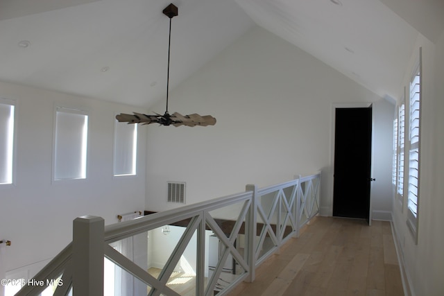 hallway with high vaulted ceiling, plenty of natural light, and light hardwood / wood-style floors