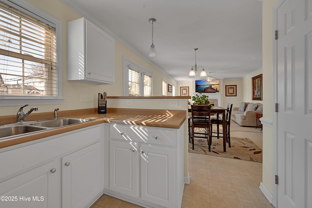 kitchen featuring white cabinetry, sink, kitchen peninsula, decorative light fixtures, and ornamental molding