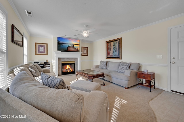 carpeted living room with ceiling fan, crown molding, and a tiled fireplace