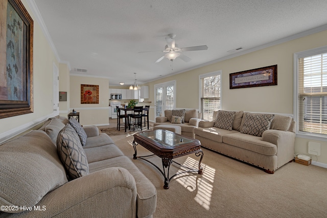 living room with ceiling fan with notable chandelier, a textured ceiling, light colored carpet, and crown molding