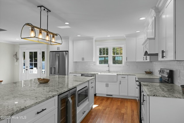 kitchen with white cabinets, decorative light fixtures, light hardwood / wood-style floors, stainless steel appliances, and beverage cooler