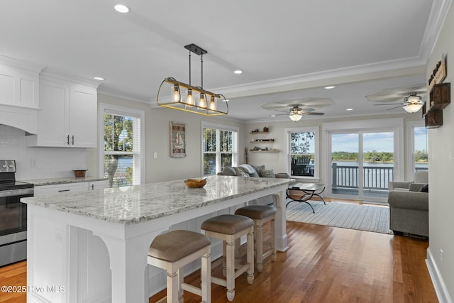 kitchen featuring white cabinets, stainless steel stove, ceiling fan, ornamental molding, and light stone counters