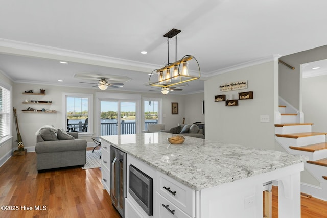 kitchen with ceiling fan, stainless steel microwave, beverage cooler, pendant lighting, and white cabinets