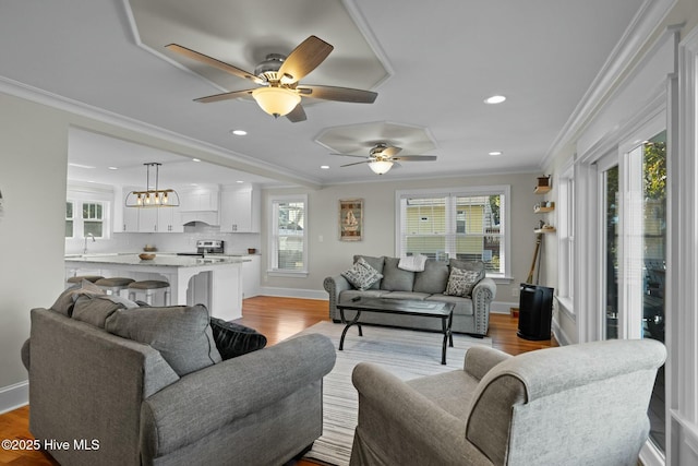 living room featuring crown molding, light hardwood / wood-style flooring, a healthy amount of sunlight, and ceiling fan with notable chandelier