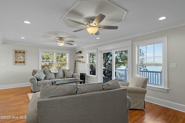 living room featuring wood-type flooring, a water view, ceiling fan, and ornamental molding