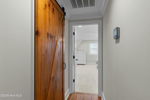 hallway with a barn door, crown molding, and light hardwood / wood-style flooring