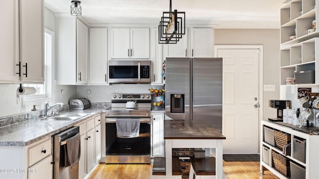 kitchen with light hardwood / wood-style floors, stainless steel appliances, decorative light fixtures, white cabinets, and sink