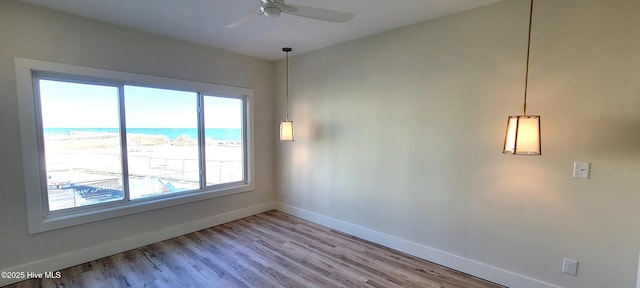 unfurnished room featuring a beach view, light wood-type flooring, a water view, and ceiling fan