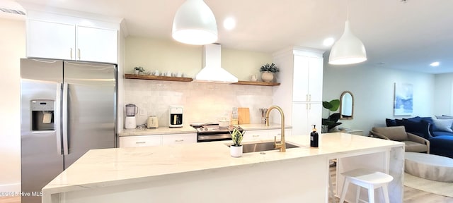 kitchen featuring light stone counters, wall chimney exhaust hood, stainless steel appliances, decorative light fixtures, and white cabinetry