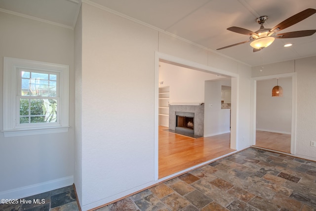 unfurnished room featuring ceiling fan, crown molding, and a fireplace