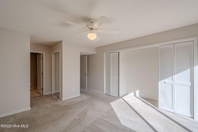 unfurnished bedroom with ceiling fan, light colored carpet, multiple closets, and a textured ceiling