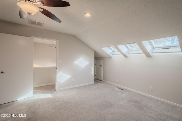 additional living space with ceiling fan, vaulted ceiling with skylight, a textured ceiling, and light carpet