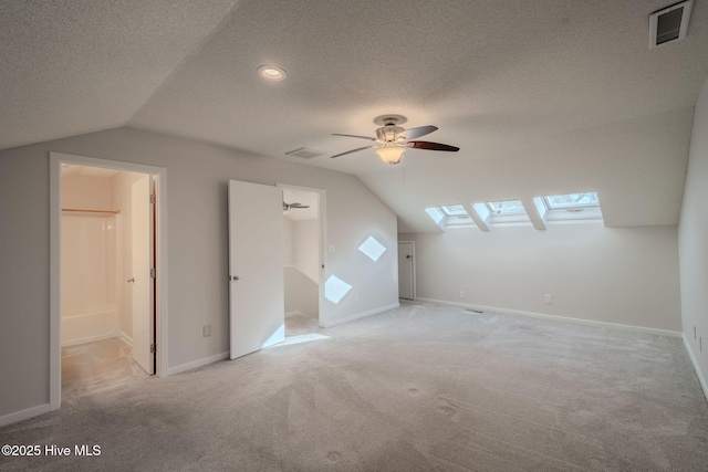 additional living space featuring a textured ceiling, ceiling fan, light carpet, and lofted ceiling with skylight