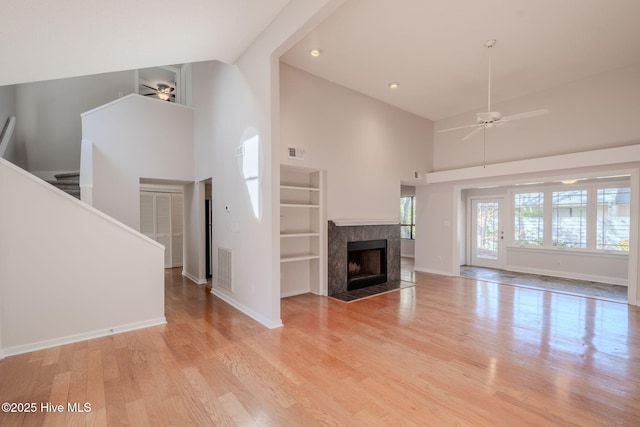 unfurnished living room featuring light wood-type flooring, ceiling fan, a high end fireplace, and a high ceiling