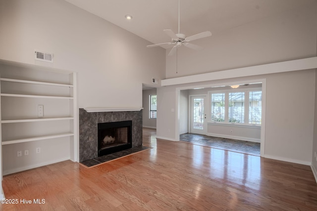 unfurnished living room with hardwood / wood-style floors, ceiling fan, high vaulted ceiling, a high end fireplace, and built in shelves