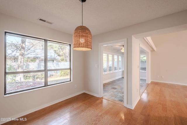 unfurnished dining area featuring ceiling fan, a healthy amount of sunlight, a textured ceiling, and light hardwood / wood-style floors