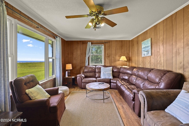 living room with a textured ceiling, light hardwood / wood-style floors, ceiling fan, and wooden walls