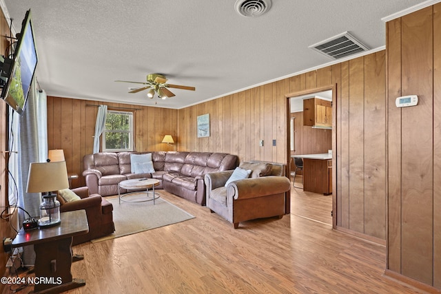 living room featuring a textured ceiling, light wood-type flooring, ceiling fan, and crown molding