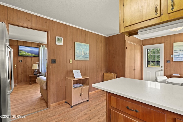 kitchen with stainless steel refrigerator, wood walls, light hardwood / wood-style floors, and ornamental molding